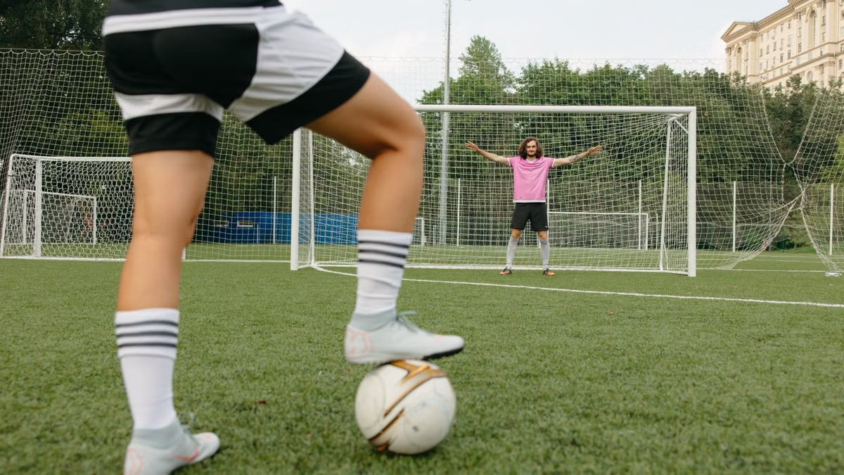 Soccer player in action aiming for the goal with a goalkeeper ready to defend.